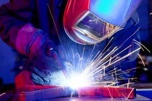 Person arc welding whilst wearing protective helmet and gloves